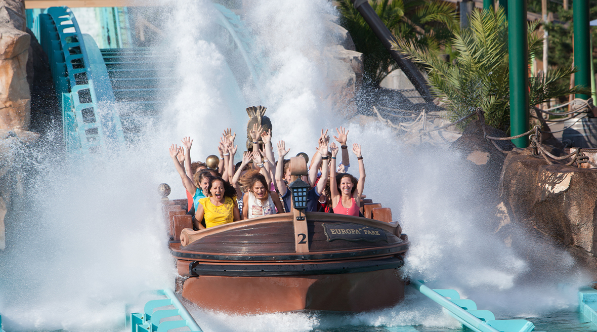 People in a water coaster ride raising their hands as their boat makes a splash